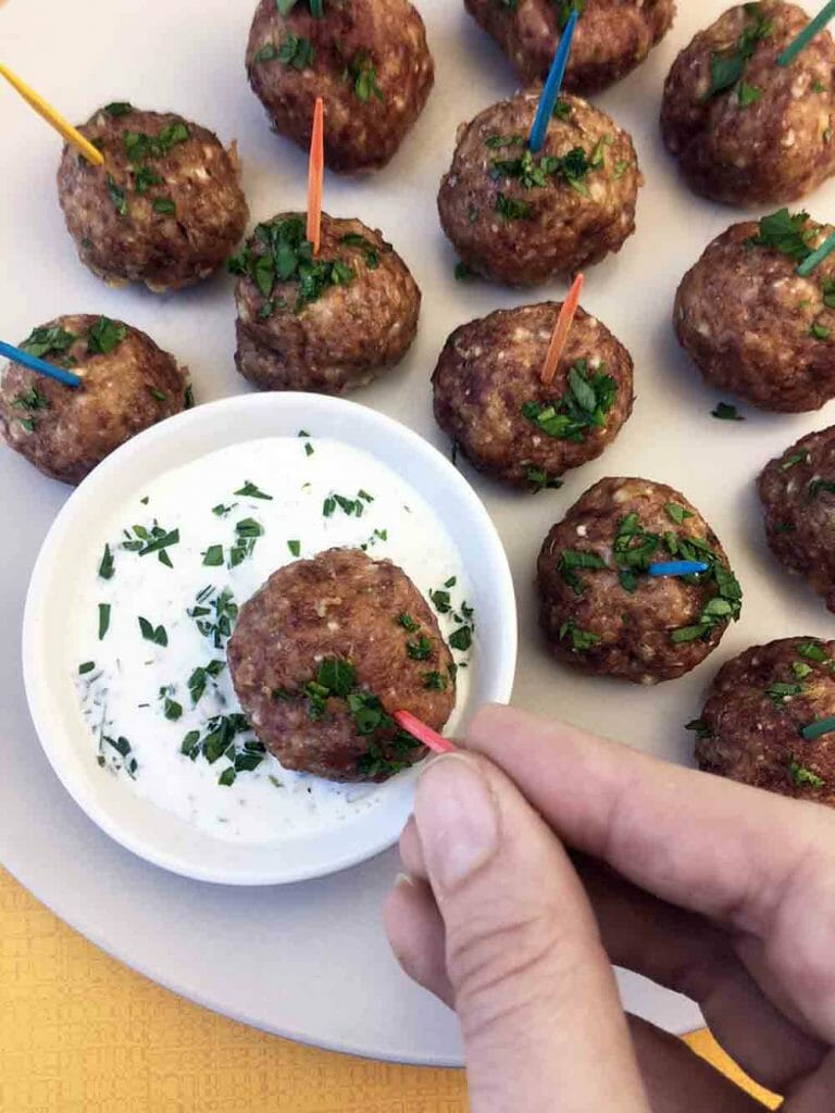 a hand dips a Greek Lamb Meatball into Tzatziki Sauce